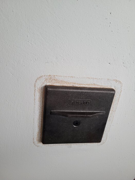 Målad skorsten med synlig spricka vid spjällreglaget, röstjärnsplatta monterad på vitmålad vägg.