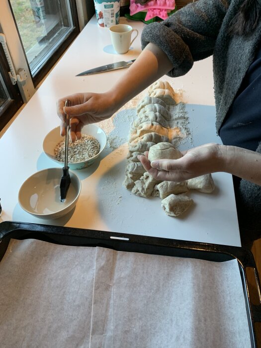 Baka havregrynsfrallor: En hand formar deg och strör havregryn, med bakplåt och bakplåtspapper redo.