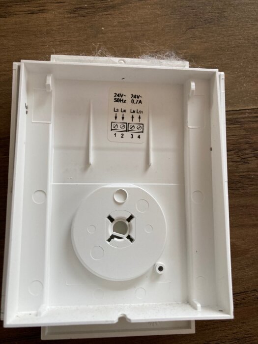 Baksida av en termostat med anslutningspunkter och märkningar för 24V, 50Hz, 0.7A, monterad på en träribba.