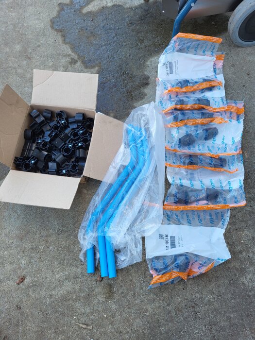 Blåa aluminiumrör för tryckluft, svart skarvkopplingar i kartong och förpackningar med kopplingar på cementgolv.