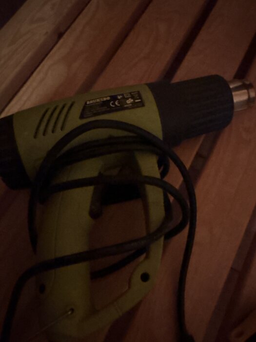 En grön och svart värmepistol ligger på en träyta.