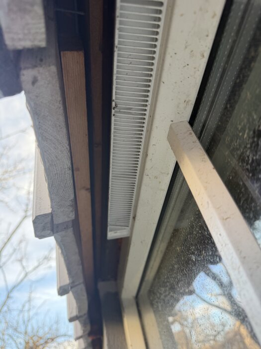 Närbild på ett fönster med synlig avsats mellan vägg och insida panel, med tydlig ventilation och trädetaljer.