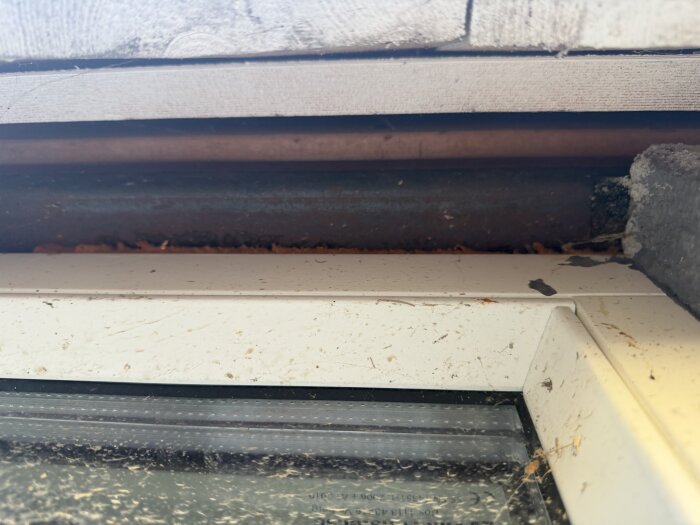 Utsida av byggnad med synlig glipor mellan vägg och fönster, där isolering diskuteras. Visar metall och trädetaljer ovanpå fönsterkarmen.