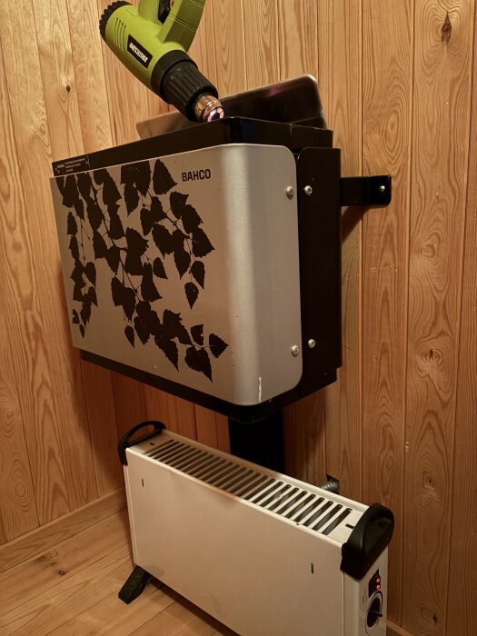 Värmepanel och värmepistol monterade på en trävägg i ett rum med panel.