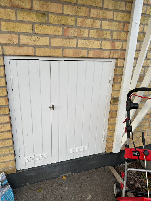 Vit träpaneldörr på en gul tegelvägg nära entrén; har ett handtag och två ventiler i nederkant.