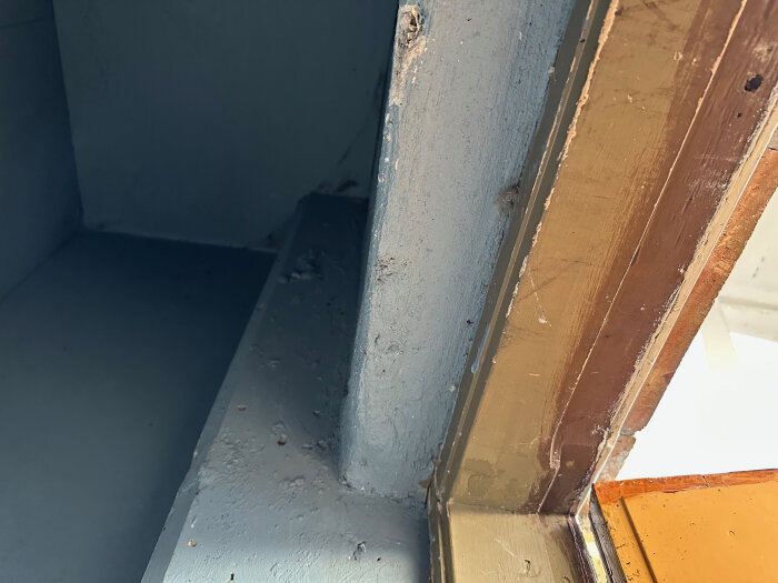 Närbild av inre vägg och dörrkarm i husets soprum, visar grov målad yta och trädetaljer intill.