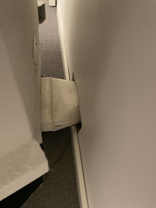Boxliknande struktur monterad på väggen, del av ventilationssystem inomhus. Trångt utrymme mellan vägg och vit låda.