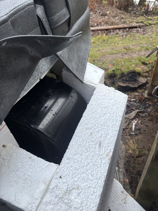 Fogskum runt en svart del av en badtunna, med stelnat skum och lös massa synlig. Omgivningen består av sten och gräs.