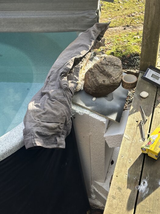 Fogskum runt en badtunna med tyg, plast, och sten som vikt, omgiven av verktyg och en kartong på trädäck.