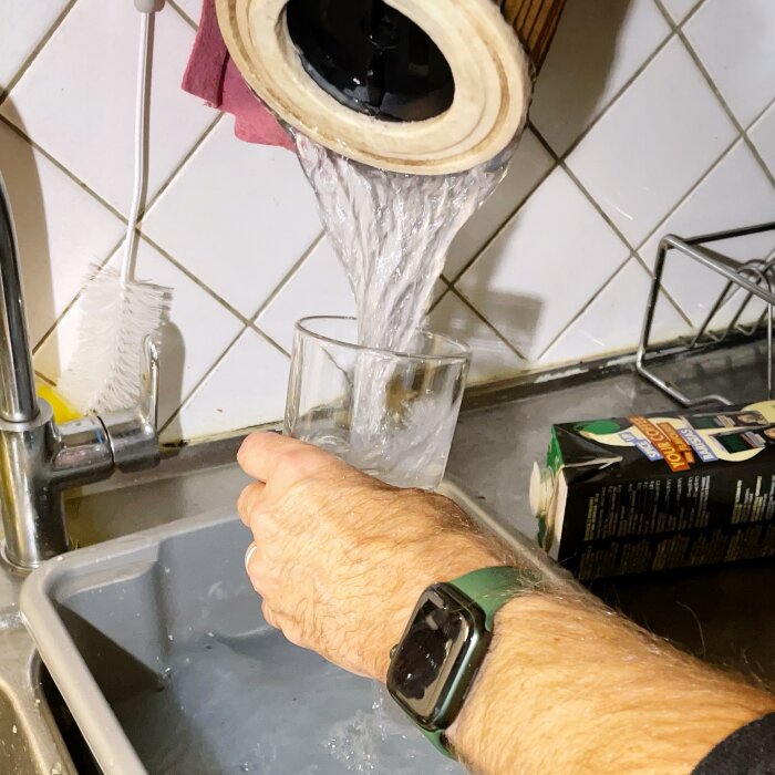 Vatten rinner genom dammsugarfilter i diskho, en hand håller i filtret. En borste och en förpackning syns i bakgrunden.