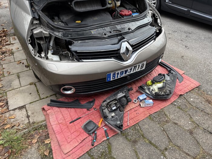 Bil med öppen motorhuv och borttagna strålkastare, verktyg och nya xenonlampor på en filt framför bilen.