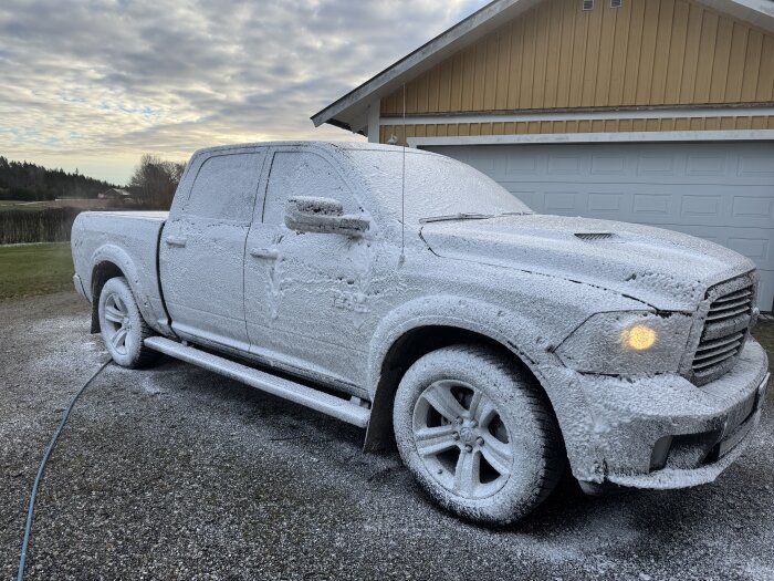 Bil täckt av vitt skum, står på en uppfart framför ett garage, förberedd för vintertvätt.