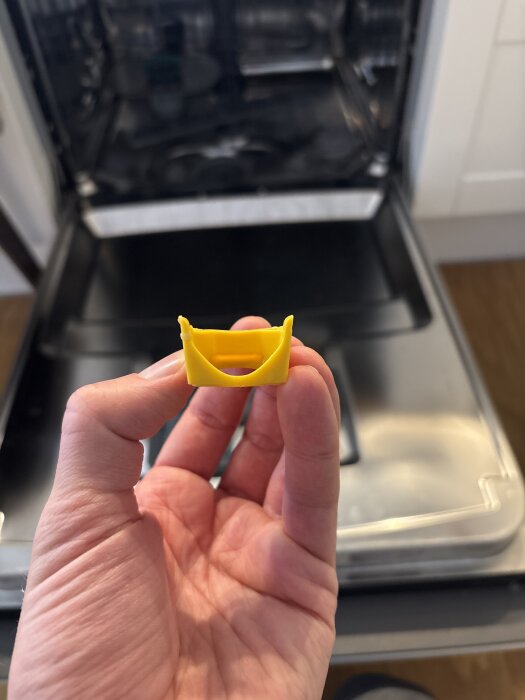 Gul backventil från Hisense diskmaskin hålls i en hand, öppen diskmaskin i bakgrunden.
