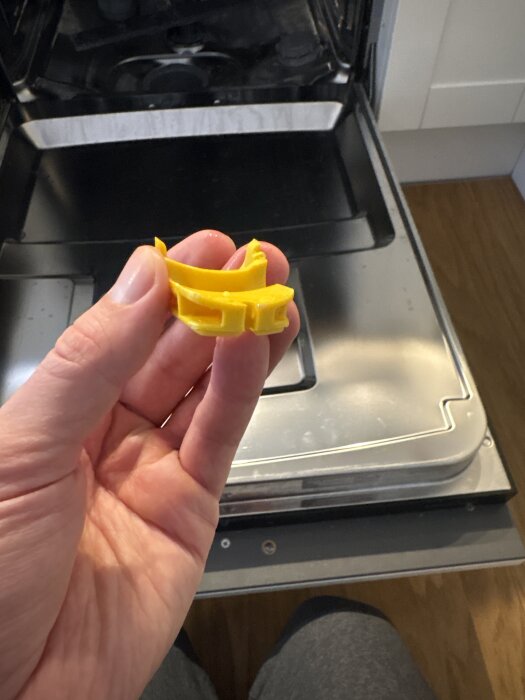 Hand håller en gul backventil framför en öppen diskmaskin, med fokus på ventilen.
