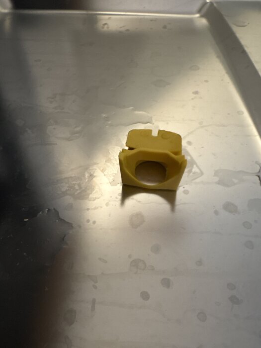 Gul backventil från Hisense diskmaskin placerad på en metallisk yta.