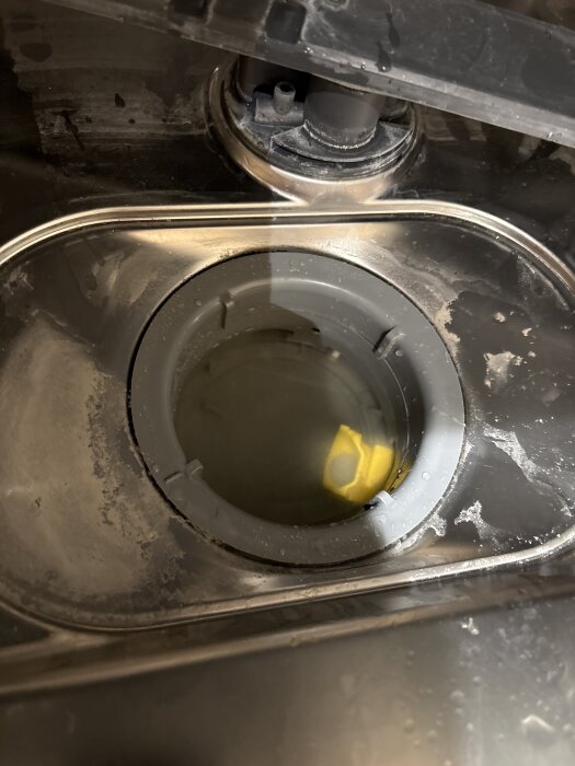 Diskmaskinsdränering med gul backventil synlig, vatten kvar i brunnen.