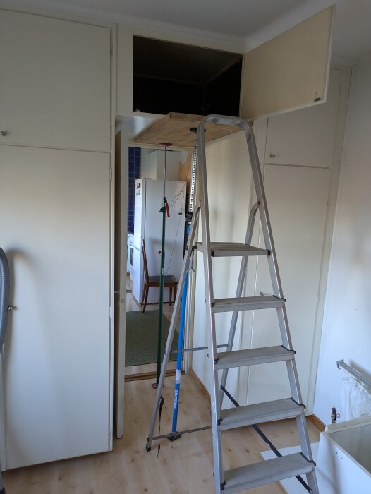 Stege står framför ett öppet skåp högt upp på väggen i ett rum, med verktyg och dammsugare i närheten.