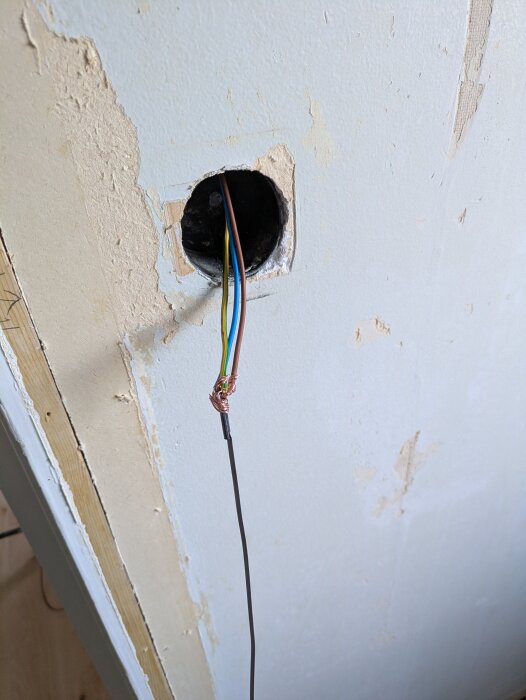 Elektriska kablar sticker ut från en rund öppning i en blå vägg med skrapad färg.