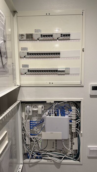 Elcentral med många kopplade kablar och brytare, inkluderar nätverksutrustning i en väggmonterad panel.
