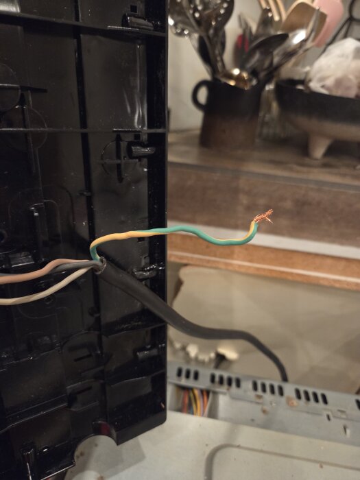 Oisolerad elledning med grön-gul kabel synlig, monterad i en svart apparatlåda, ligger på en arbetsyta i ett kök.