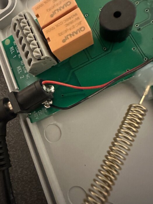 Närbild av lödda kablar från Shelly Uni Plus anslutna till reläge på ett kretskort med orange komponenter och svart cylinderformad del.