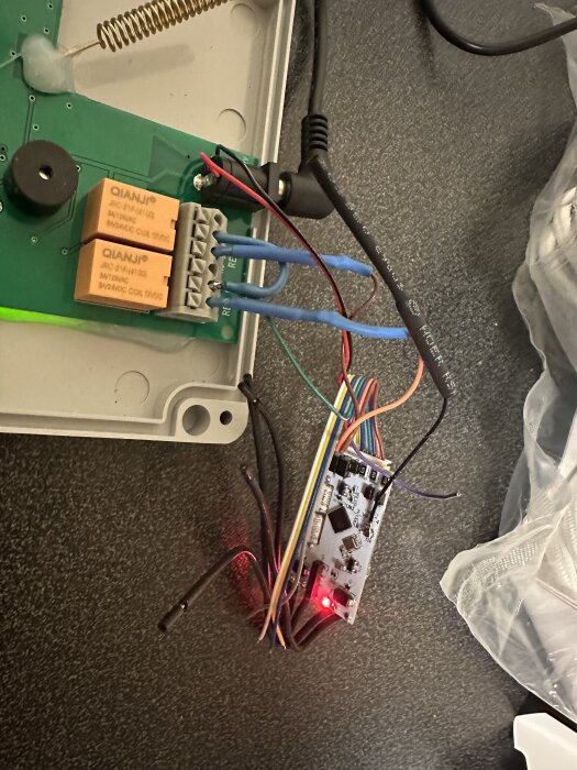 Shelly Uni Plus kopplad till ett larmsystem, med kablage, lödningar och en tänd lysdiod synliga på ett kretskort.