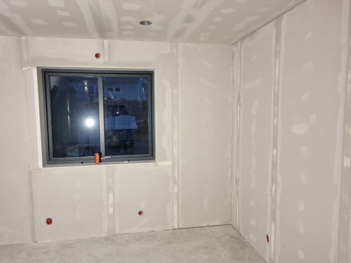 Ett rum med nyligen spacklade gipsväggar och ett fönster, förberett för renovering. En läskburk står på fönsterkarmen.