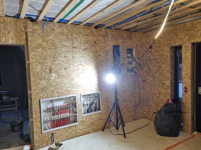 Renoveringsprojekt i hall med OSB-väggar, spotlights och elinstallationer synliga. Verktyg och byggmaterial runtom.