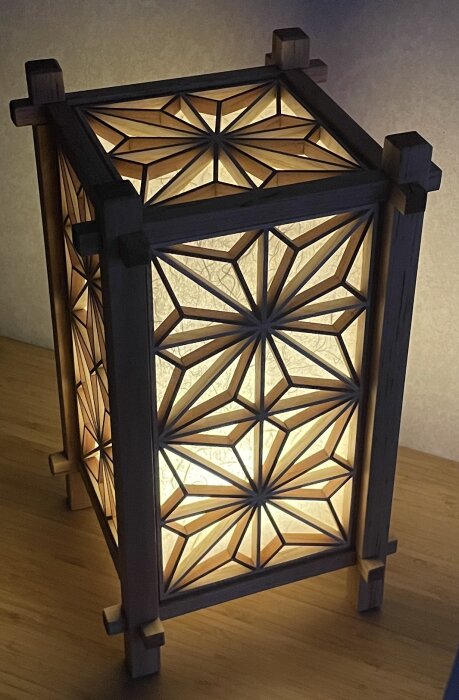 En dekorativ lykta med kumikomönster och ljus inuti, placerad på ett trägolv.