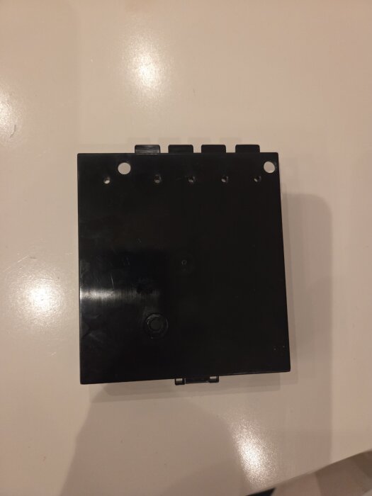 Svart plasthölje med flera små hål längs överkanten, placerat på en ljus yta.