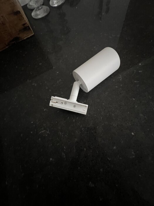 Vit spotlight med monteringsskena, placerad på en mörk yta, redo för installation och inkoppling.
