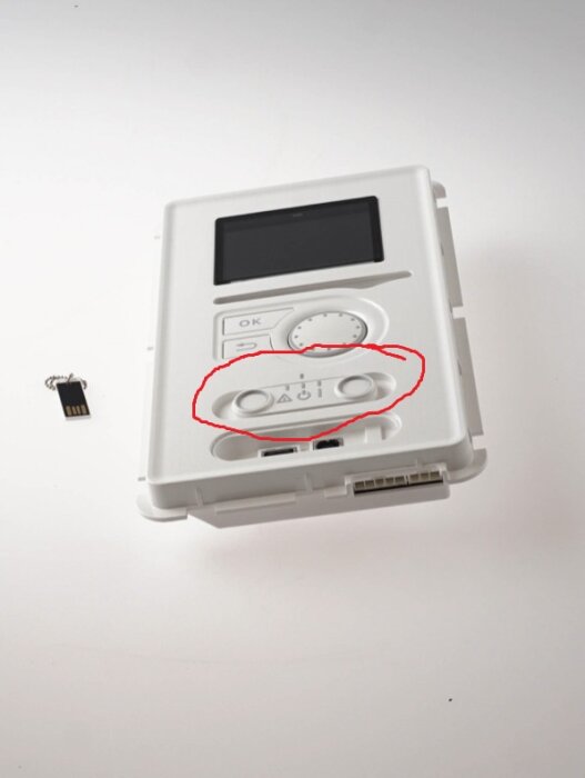 Bild av en elektrisk panel med en inringad sektion med tre symboler och knappar, föremålet till vänster är ett USB-minne.