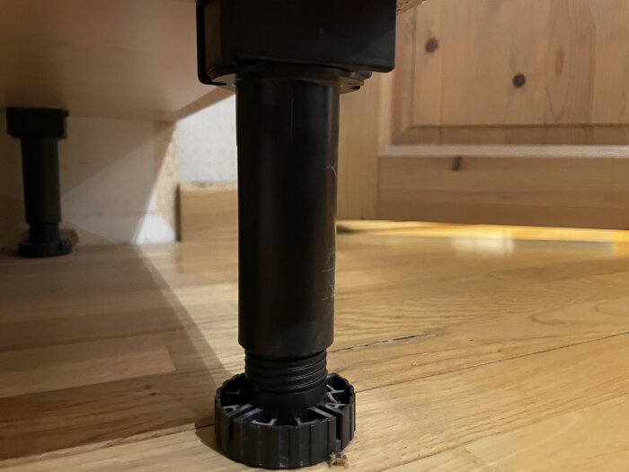 Svarta justerbara ben under köksskåp, monterade på trägolv.