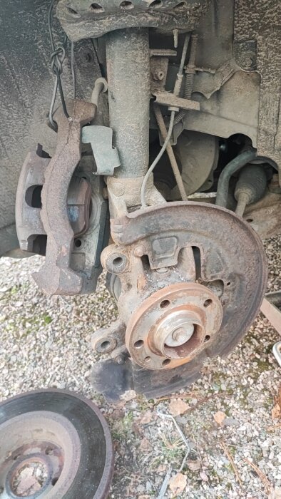 Bild av en bils bromsskiva och bromsok under byte av skivor och belägg, med demonterade delar på marken.