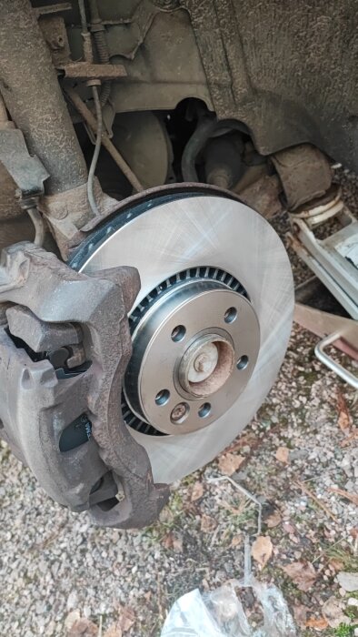 Bils bromsrotor och bromsok monterade under byte av skivor och bromsbelägg, del av ett reparationsprojekt.