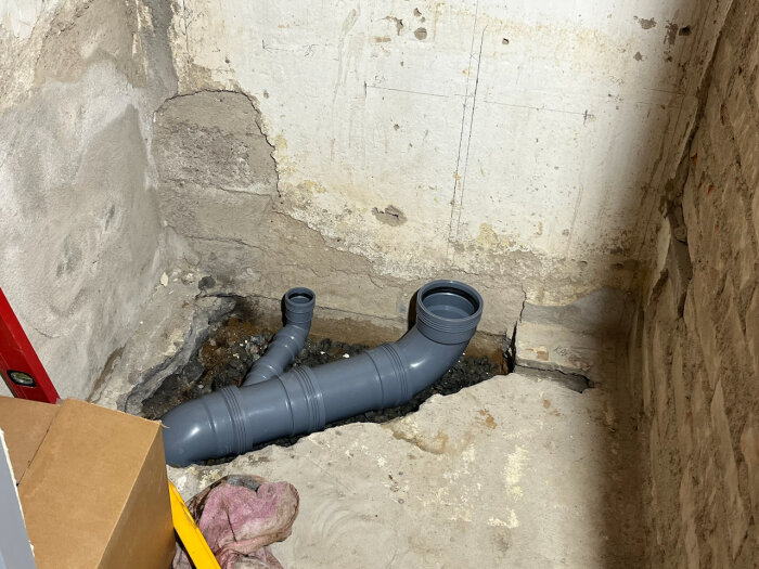 Gråa plaströr installerade i hörnet av ett rum med gamla murade väggar och en cementgolv, under renovering.