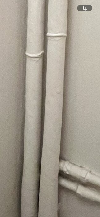 Två rör med vit isolering, misstänkt asbest, synliga på en vit vägg. Baksidan visar ett nätliknande mönster.