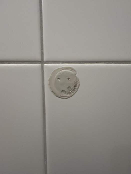 En rund uttagning i ett kaklat badrumsvägg, med limrester och en cirkulär markering synlig. Eventuellt för elinstallation.