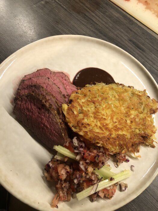 Älginnanlår med pepparsås och råraka på en tallrik, serverat med en tomat- och rödlökssallad.