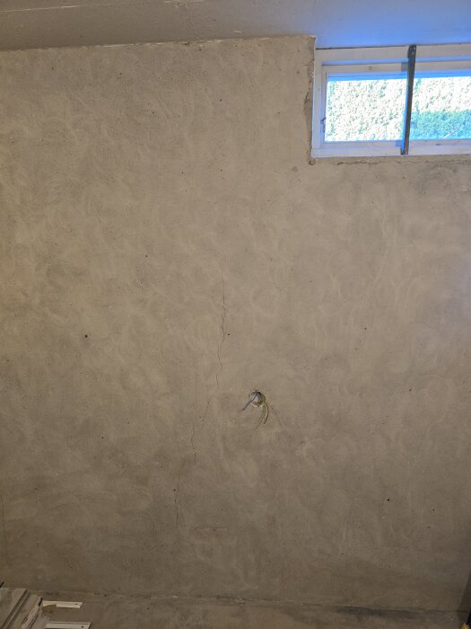 Betongvägg med sprickor och en oisolerad eldosa med kablar, belyst av ett fönster längst upp.