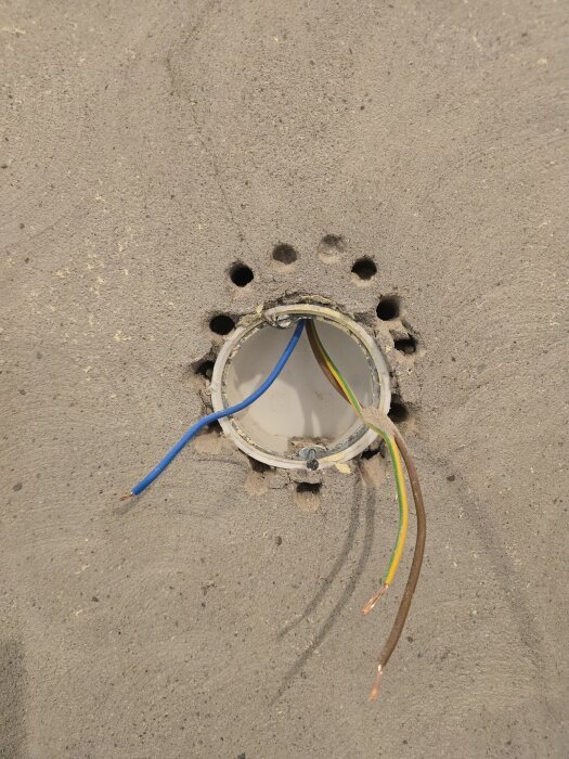 Elektrisk dosa i en murad vägg med exponerade kablar och flera borrade hål runt om.