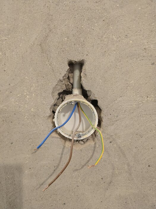 Öppnad eldosa i betongvägg med exponerade elektriska ledningar i blått, brunt och grönt/gult samt ett VP-rör som går uppåt.