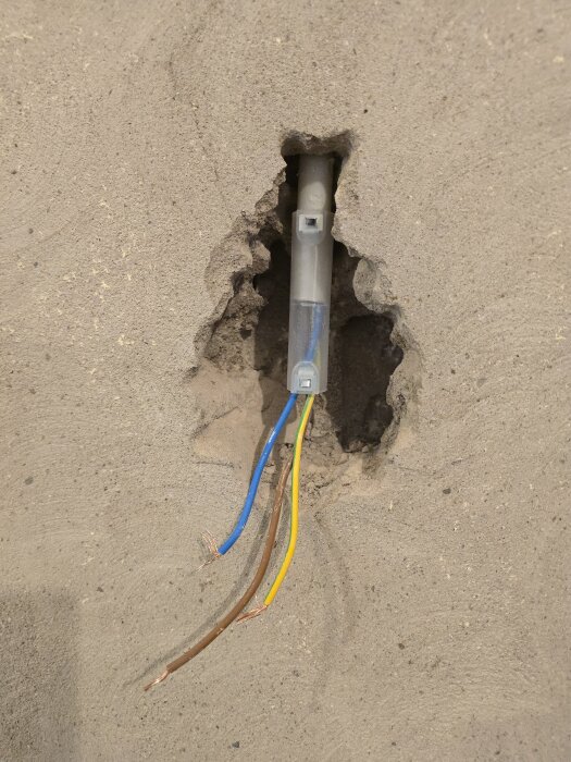 Utsatt eldosa med synliga kablar i väggen, omgiven av håltagning i betong.