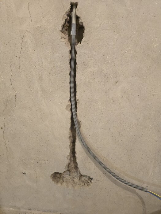Flexrör installerade i spår i betongvägg för eldragning, med oregelbunden form på väggen.