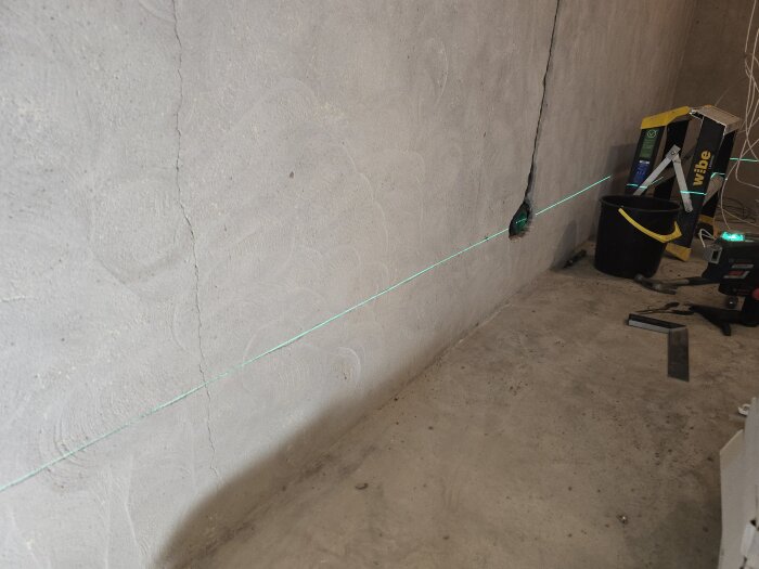 Betongvägg med spricka, laserlinje markerar eldragning för nya uttag, verktyg och utrustning vid sidan.