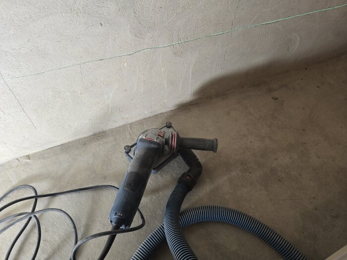 Vinkelslip med dammsugarslang på golvet vid vägg med markerad linje.