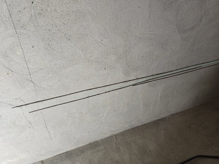 Spår för elinstallation i en putsad murvägg med två parallella snitt, del av renoveringsprojekt i ett hemmagym.