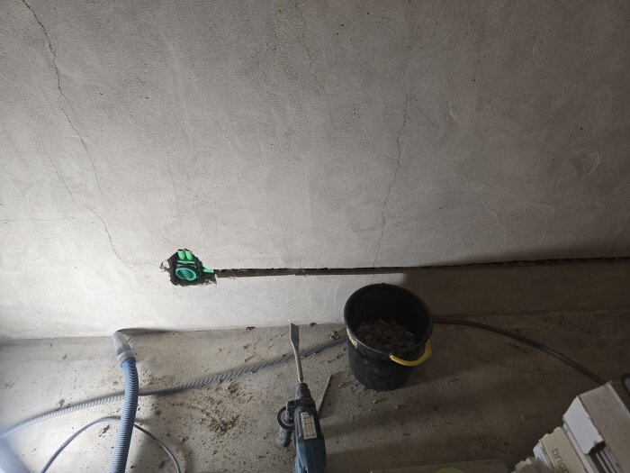 Vägg med nyinstallerad Multifix-dosa och spår för elsladdar. Verktyg och kabel på golvet med en hink fylld med skräp.