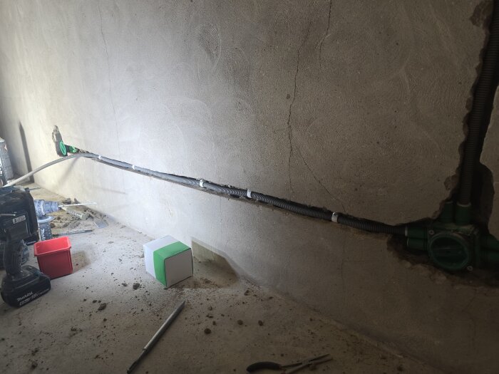 Vägg med synliga sprickor och nylagda flexrör för elinstallation; verktyg, damm och låda på golvet.