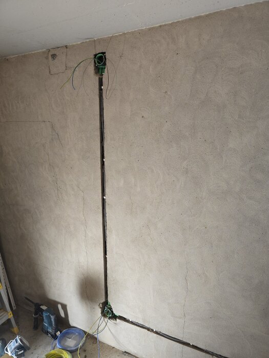 Vägg med fräst spår för elinstallation, synliga dosor och ledningar. Verktyg och material på golvet.